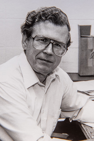 black and white photo of Frank Collins wearing glasses and sitting at a desk