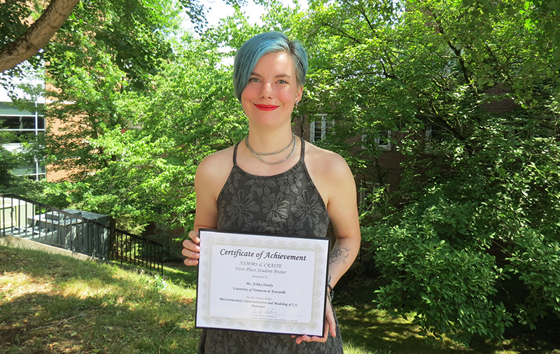 photo of Ashley Handy holding certificate, trees in background