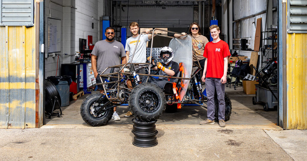A team of MABE students stand by their vehicle they will be riding in the Baja SAE Competition.